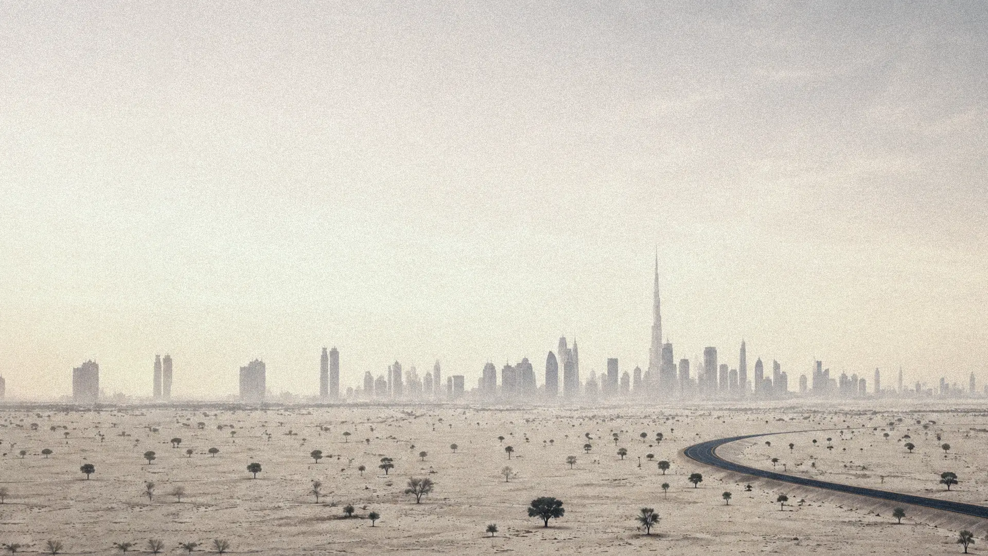 Dubai skyline seen from the desert across an open plain with a road leading toward the city